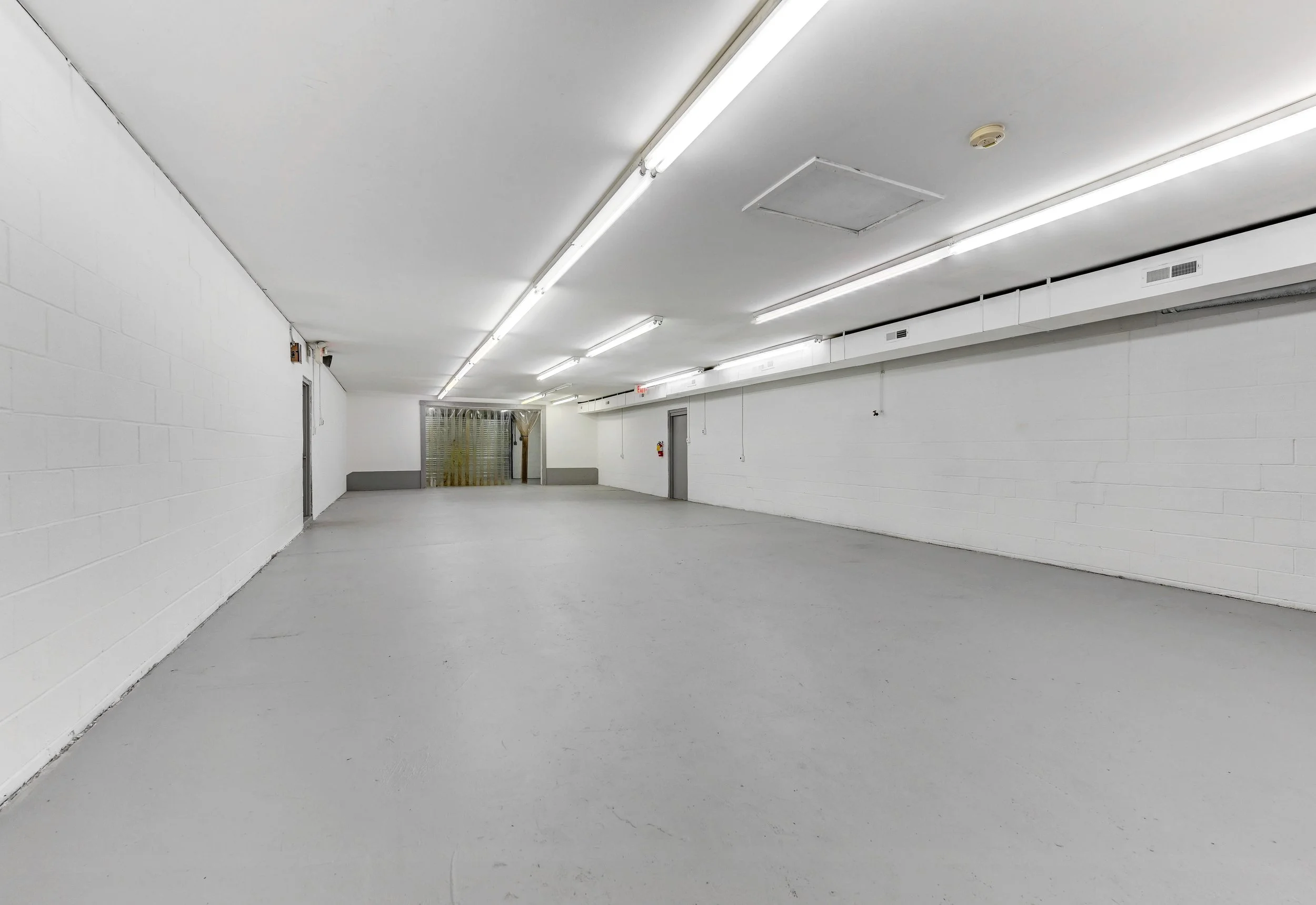Empty underground parking garage with white walls, gray floor, and fluorescent lighting.