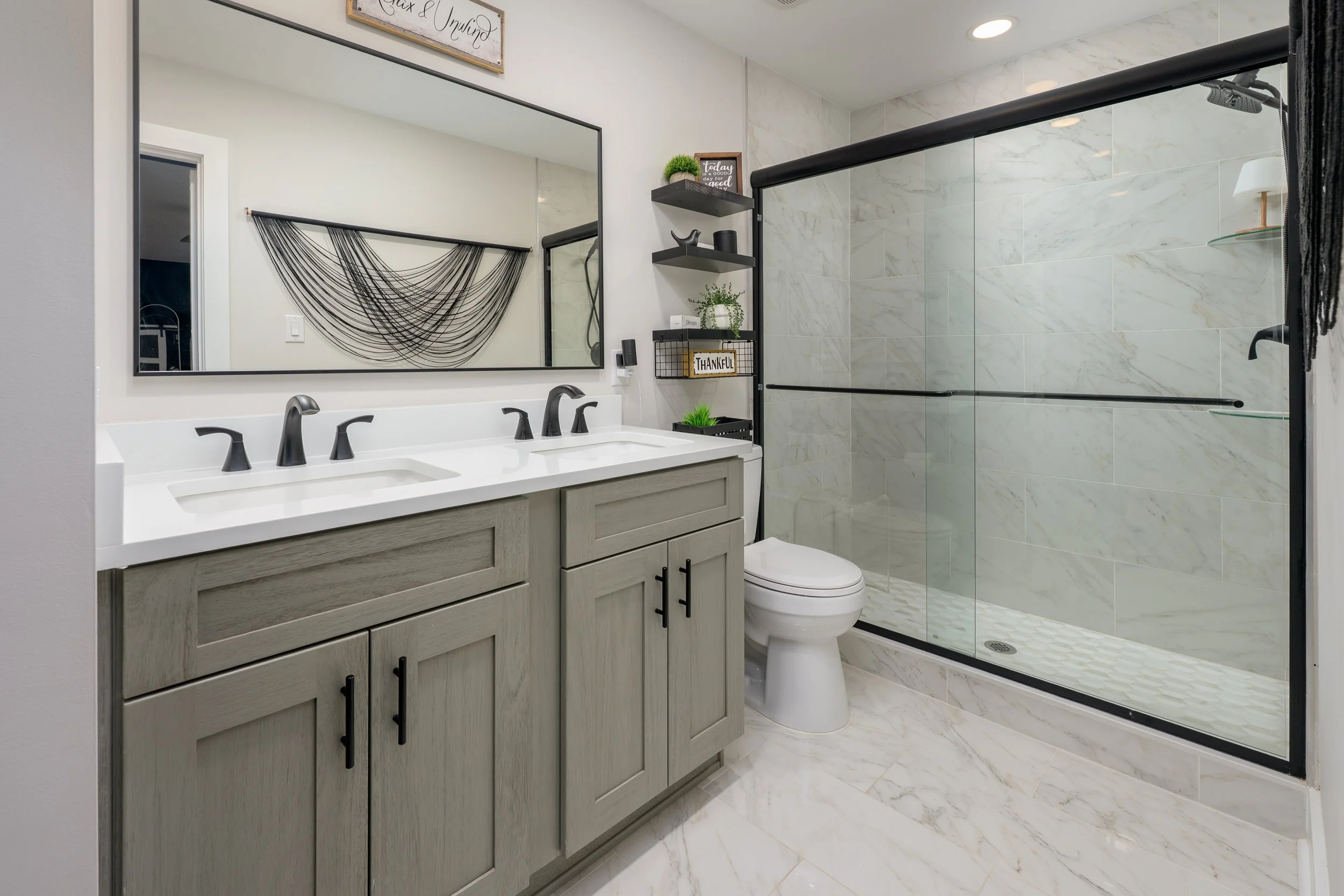 Modern bathroom with double vanity, large mirror, and glass-enclosed shower with marble tiles.
