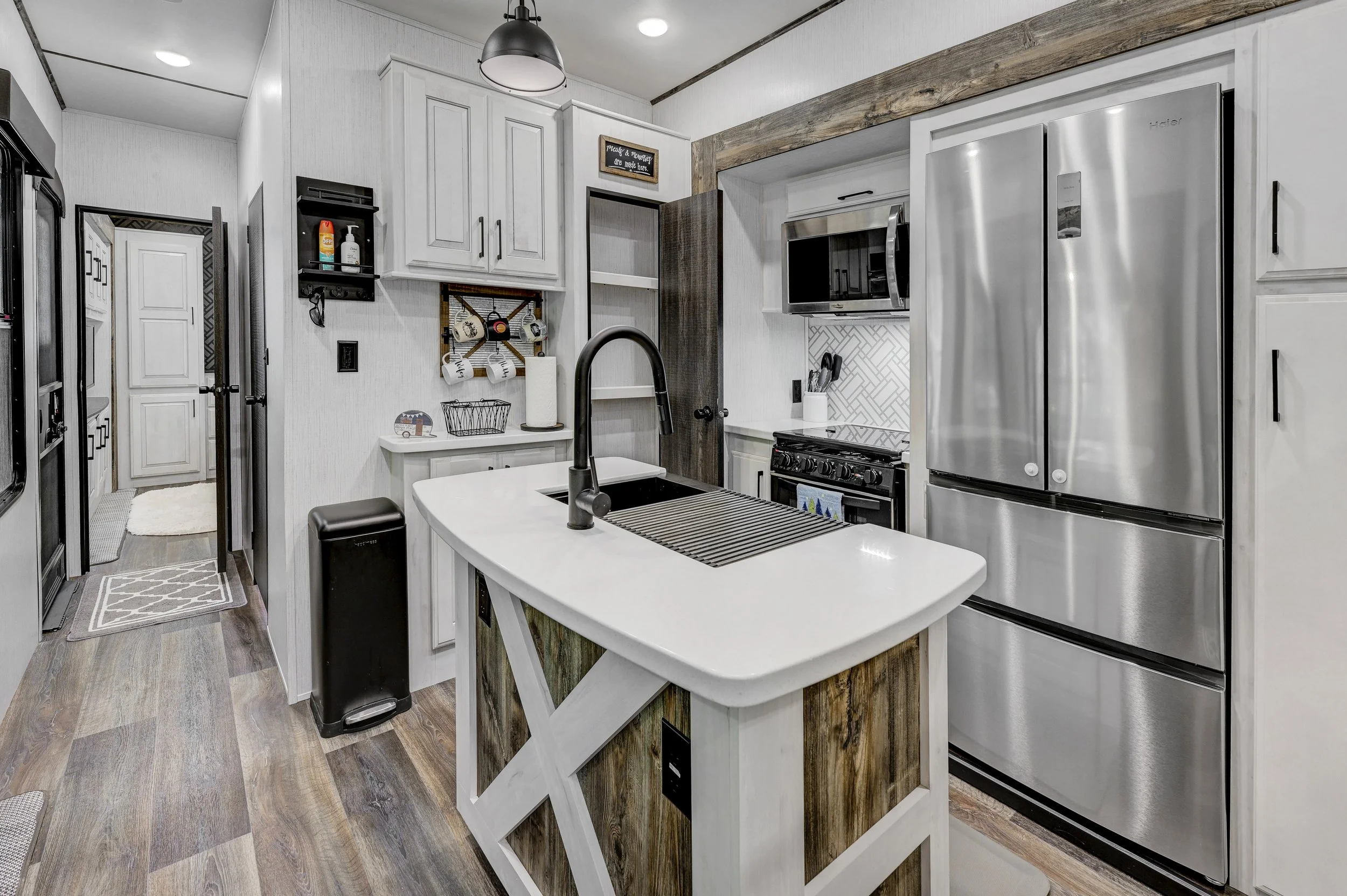 Modern kitchen with white cabinets, stainless steel refrigerator, black stove, microwave, wooden accents, and island with sink.