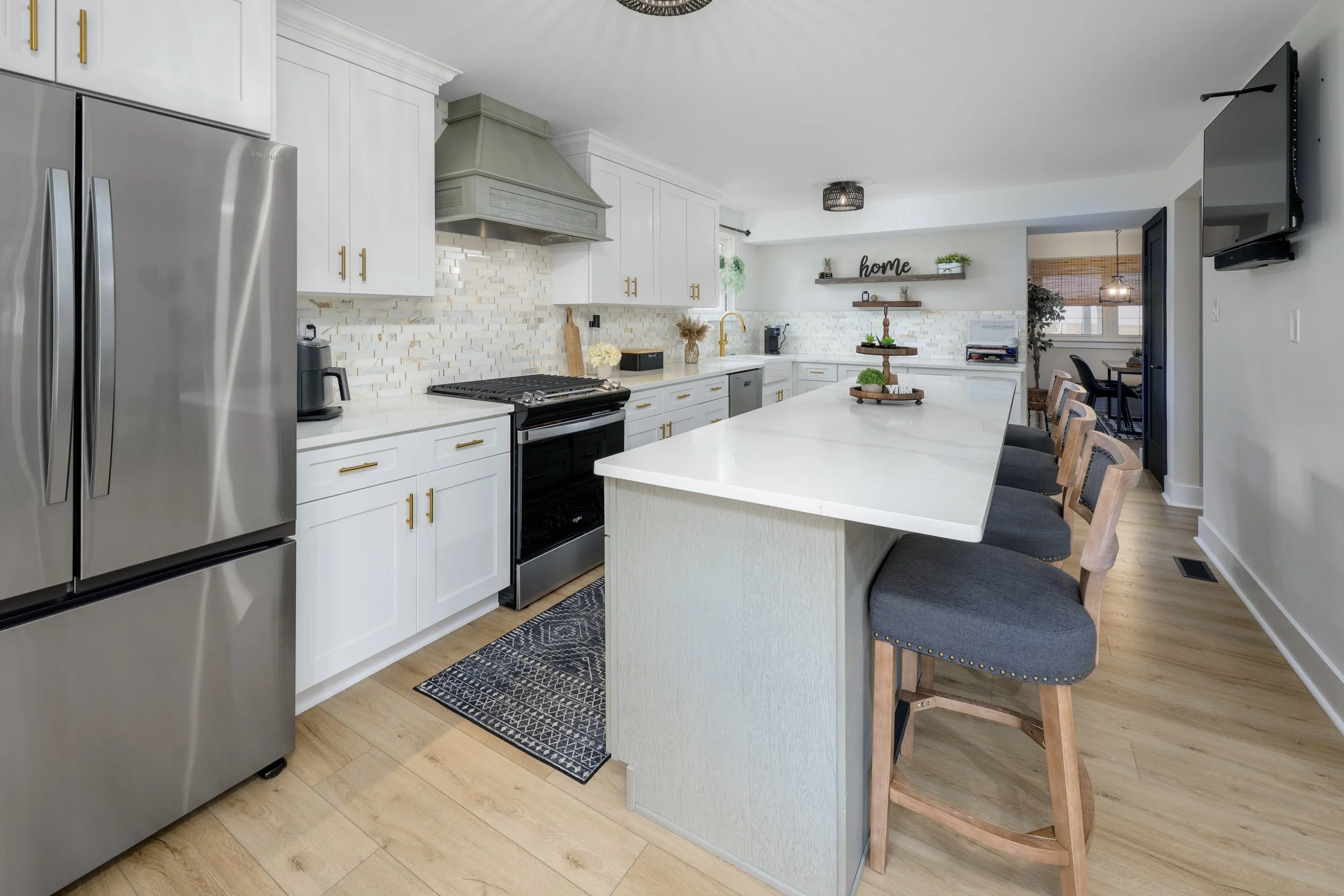 A modern kitchen with white cabinets, a large island with bar stools, stainless steel appliances, and wood flooring.