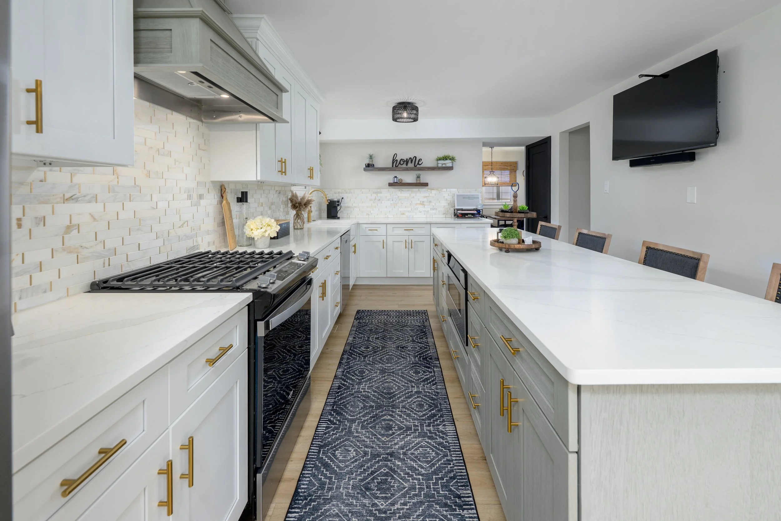 Modern kitchen with white cabinets, gold hardware, black appliances, marble backsplash, and a long island with seating