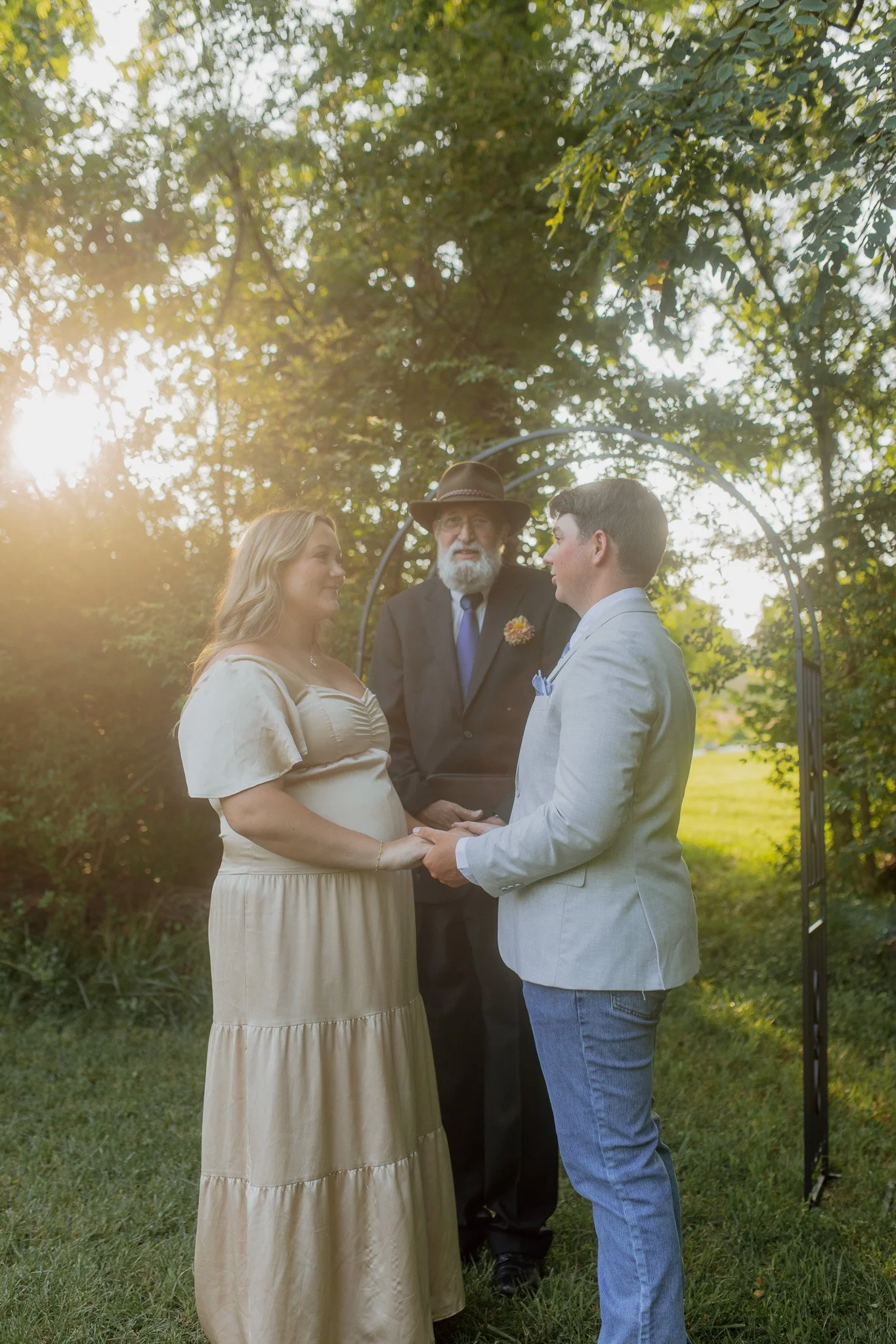 A couple marries in a wooded area with a metal arch in the background