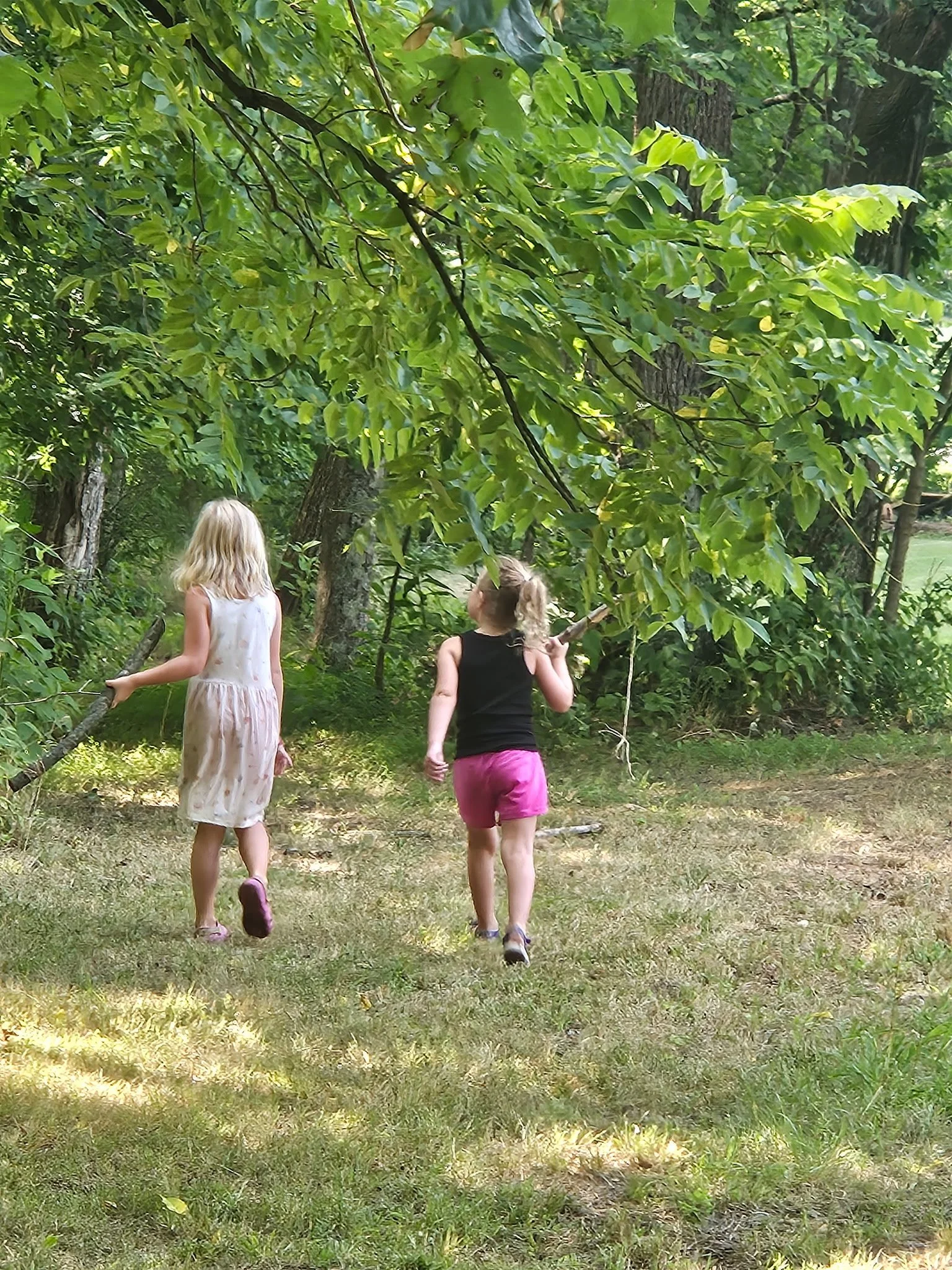 two little girls wander the field beside trees