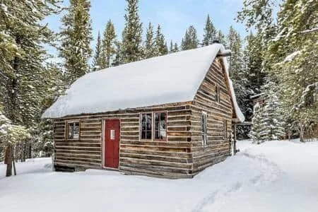 Log cabin covered in snow surrounded by pine trees in winter