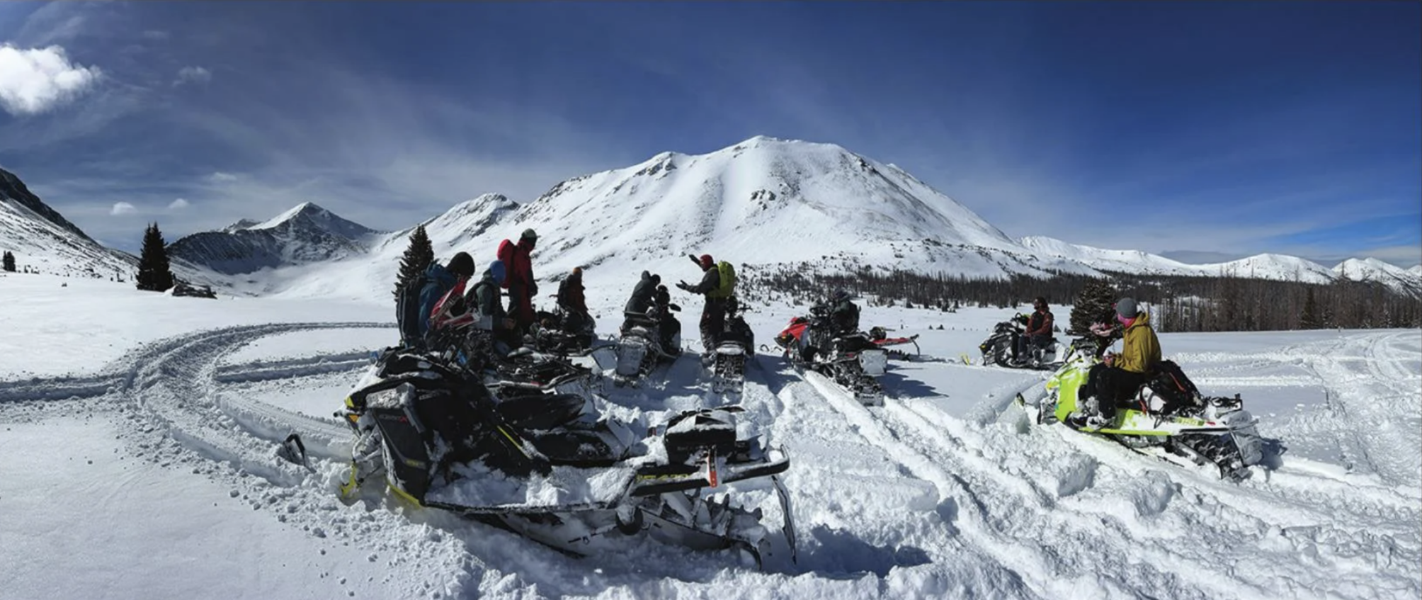 A group of snowmobile riders gathered in circle at the base of a mountain to discuss avalanche education during an AIARE 1 avalanche course taught by Powder Pro Lab near Leadville, Colorado.