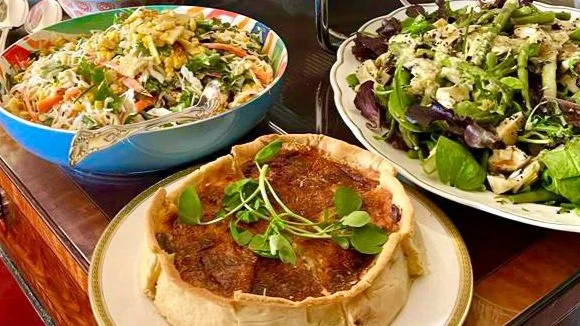 A meal with a deep-dish pizza topped with herbs in the foreground, and two salads; one with greens and vegetables, and another with pasta, vegetables, and shredded cheese.