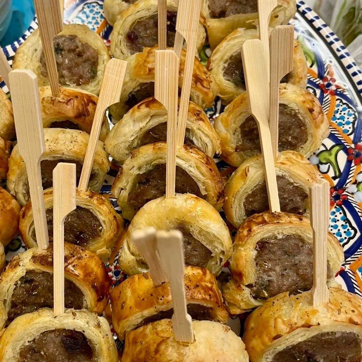 Close-up of puff pastry pinwheels with meat filling, served on a decorative plate with wooden skewers.