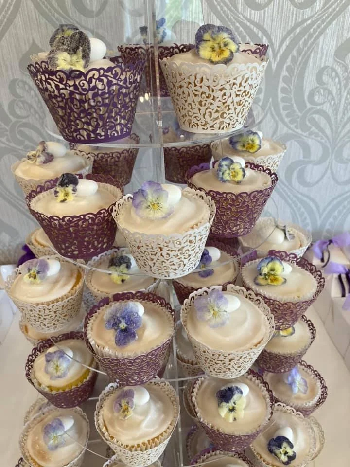 Display of cupcakes in decorative wrappers with edible flowers on top, arranged on a tiered stand.