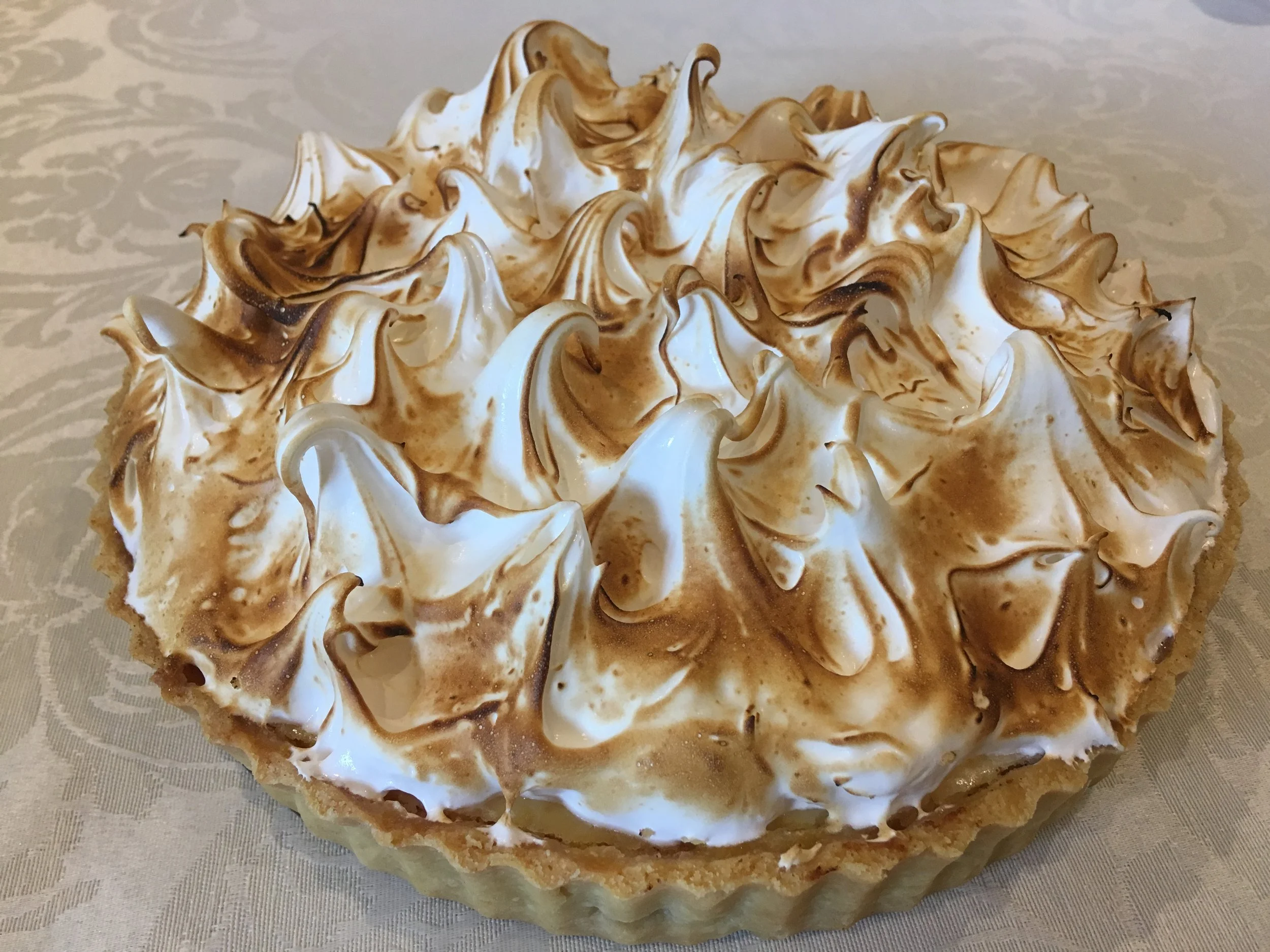 A toasted meringue pie topped with toasted meringue peaks and a caramel drizzle.