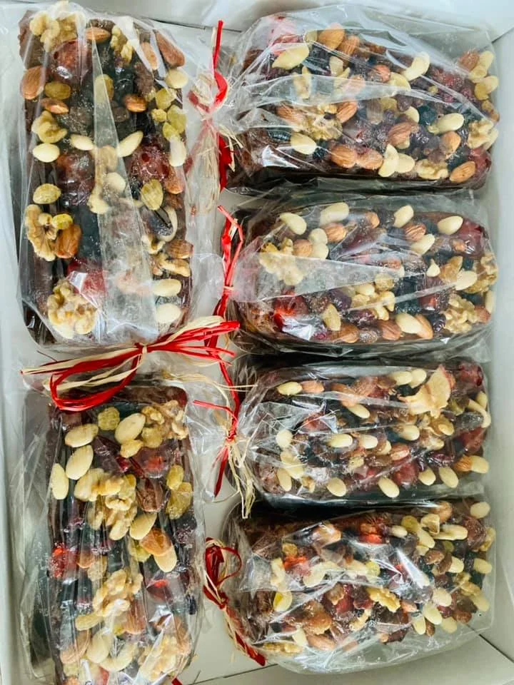 Bundles of prepackaged mixed dried fruit and nuts wrapped in clear plastic and tied with red twist ties inside a box.
