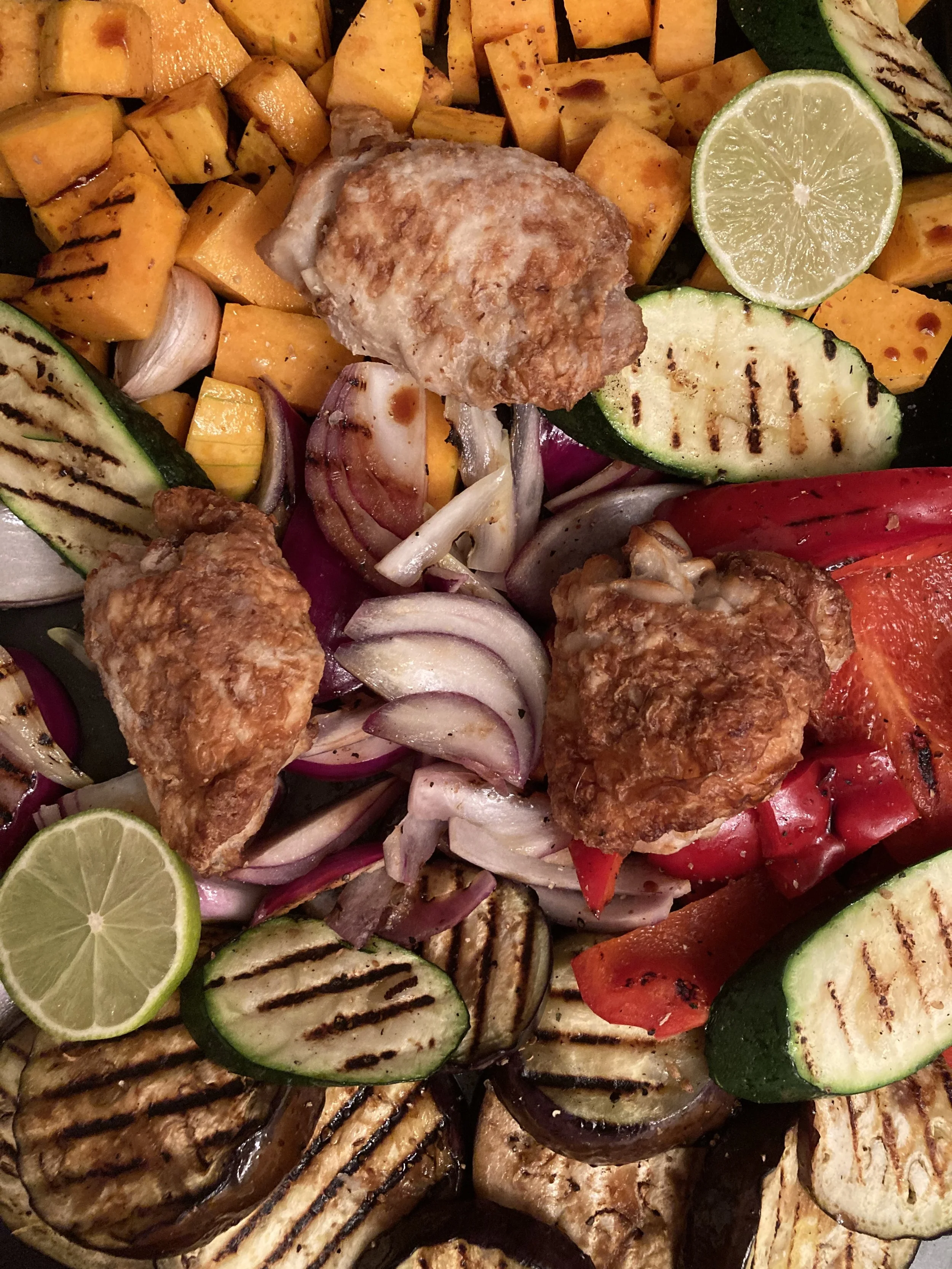 Grilled vegetables with chicken nuggets, lime wedges, and grilled zucchini, eggplant, red bell peppers, onions, and butternut squash.