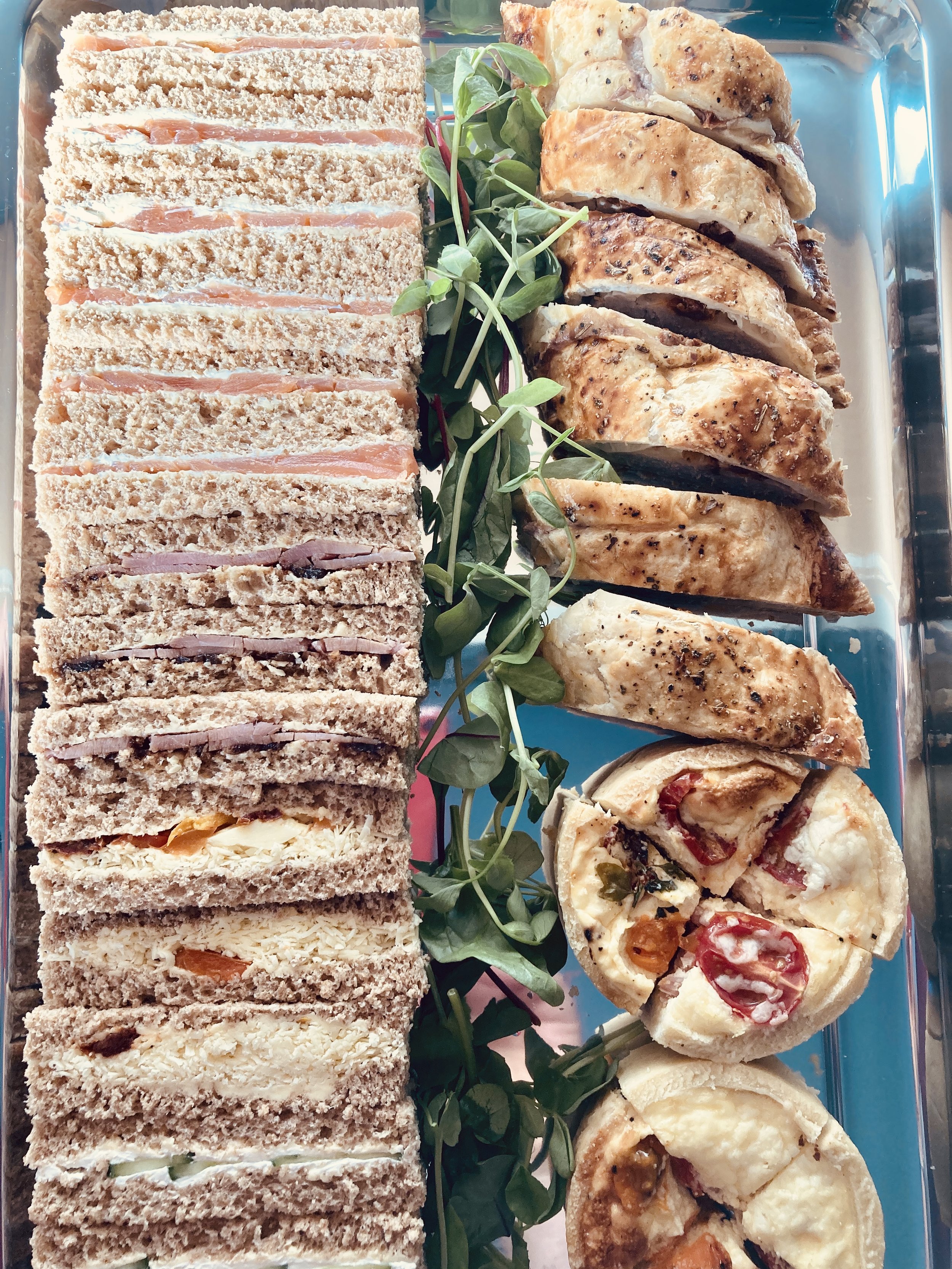 A platter with various small sandwiches, roasted chicken pieces, and mini pizzas, with garnish of microgreens.