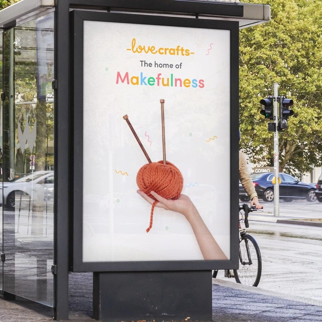 Bus stop shelter with a large advertisement showing a hand holding a ball of yarn with knitting needles, promoting crafts and mention of makefulness.