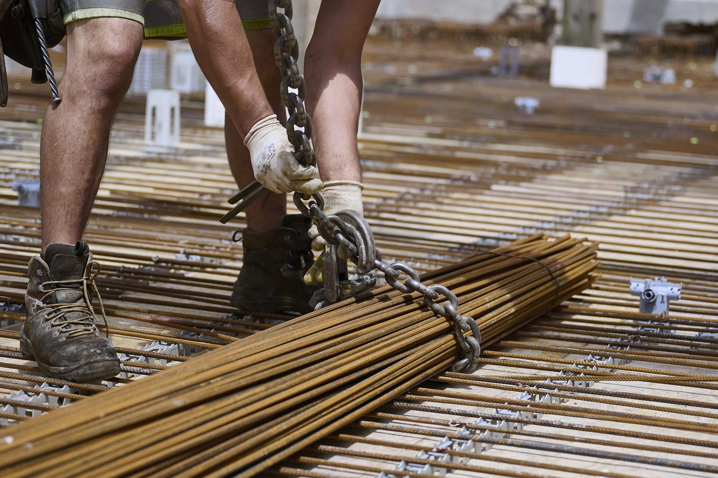 Ouvrier déplaçant un fagot de barres d'armature à la chaîne sur un chantier, photographie de chantier à Neuchâtel