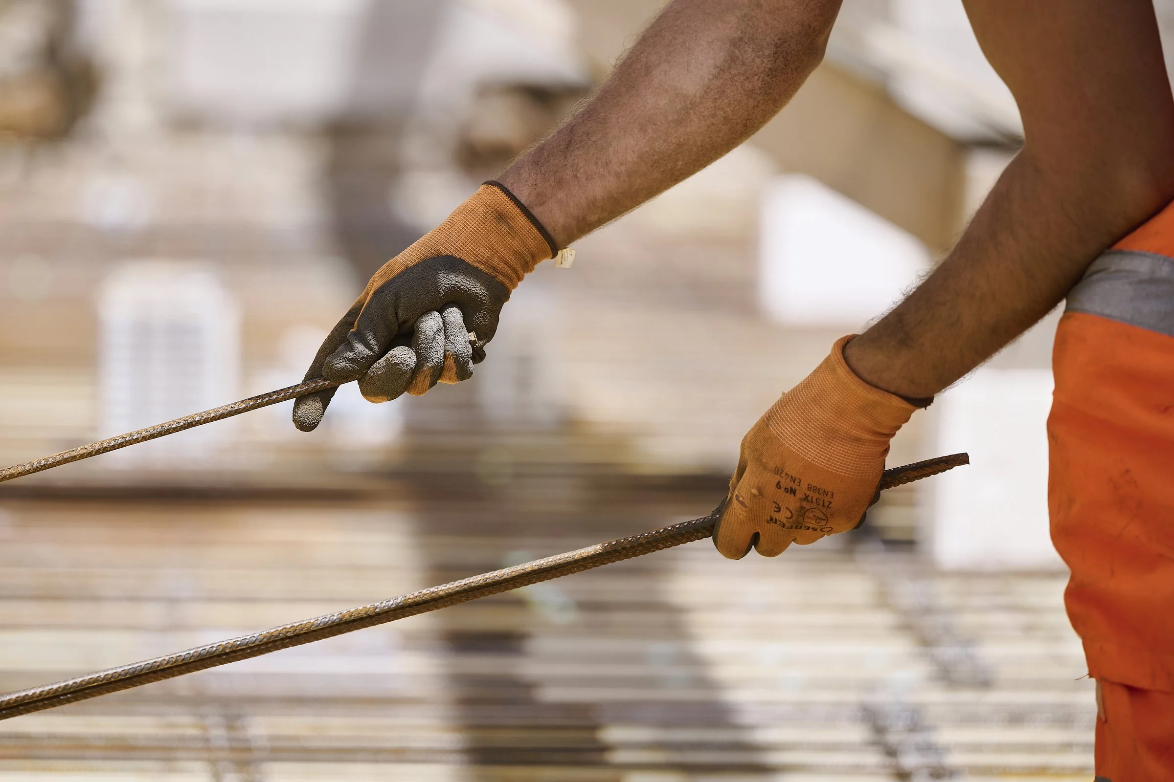 Mains gantées manipulant une barre d'armature sur un chantier, photographie de chantier à Neuchâtel