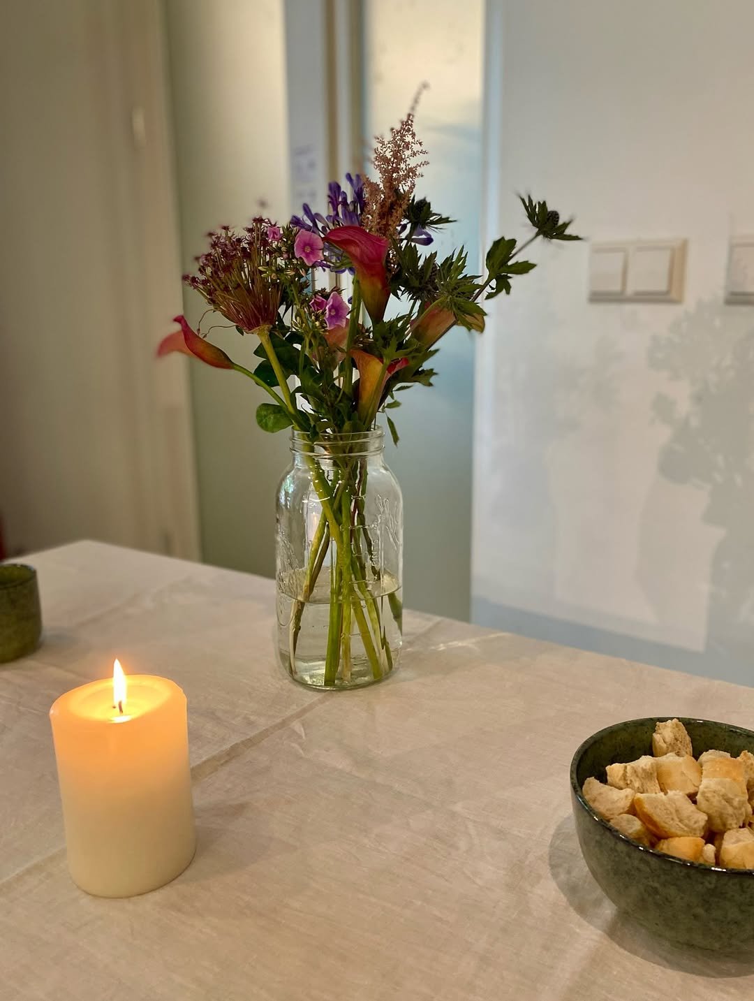 The Lord's Supper table at our English-speaking church Berlin, featuring a colorful flower bouquet, a lit candle, and communion bread in a black bowl during Sunday service.