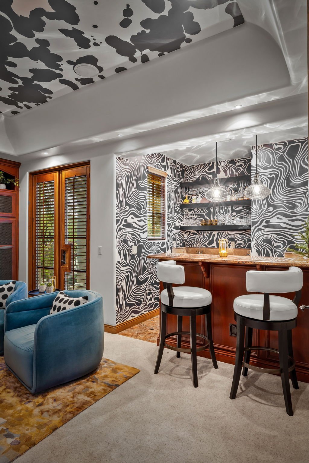 Custom home bar with dark wood cabinetry, swirl-patterned wallpaper, and cowhide ceiling accents in Superstition Mountain, designed by Red Carrot Design.
