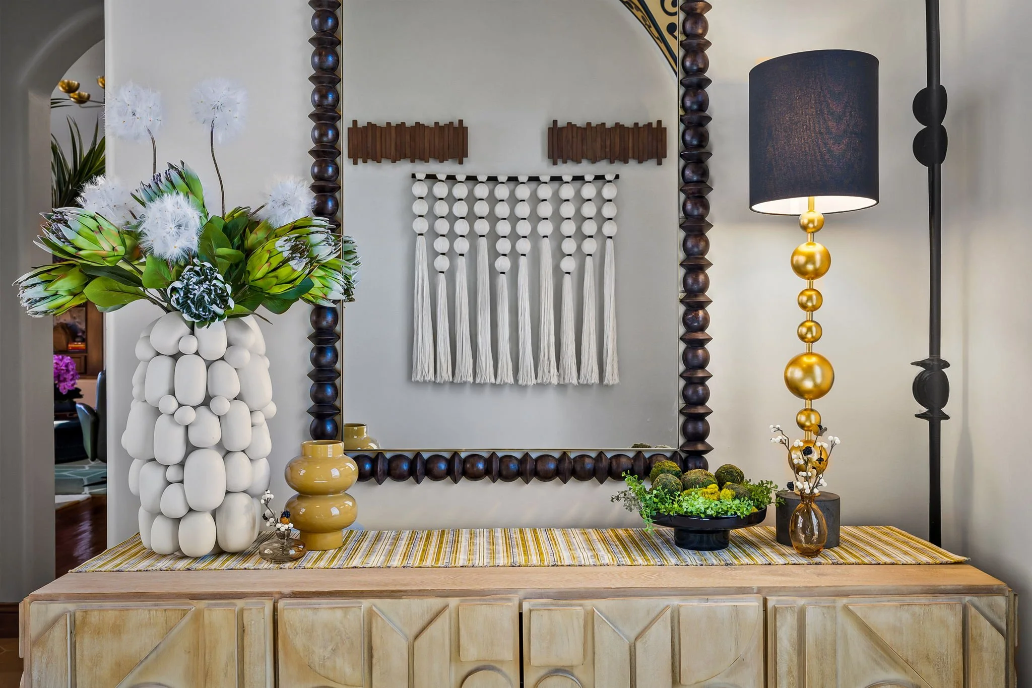 Eclectic entry sideboard styling in Gold Canyon, AZ, featuring a textured white vase, gold ball lamp, and beaded wall art curated by Red Carrot Design.