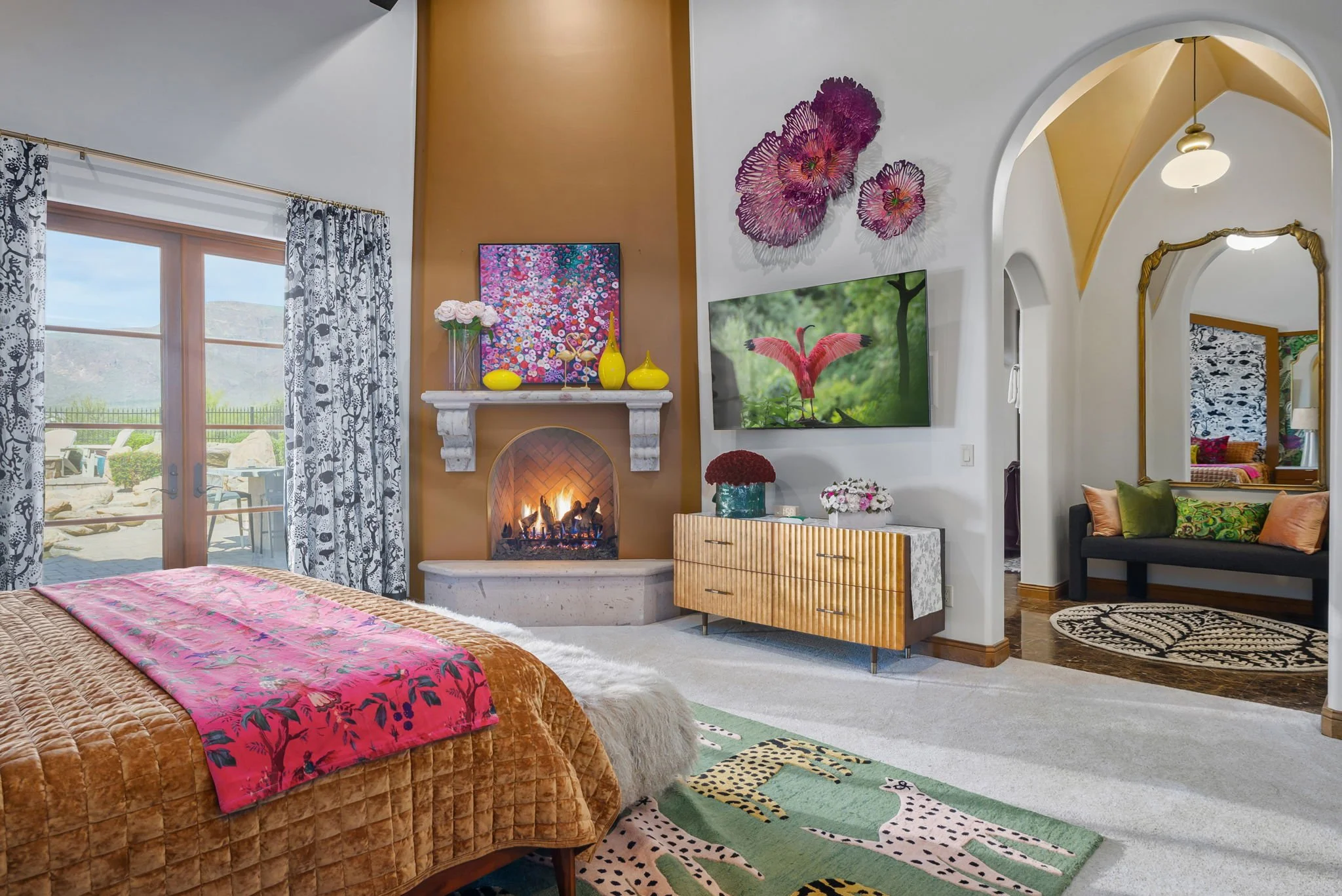 Luxury primary bedroom with a corner stone fireplace, copper-toned accent wall, and mountain views in Superstition Mountain Golf Community.