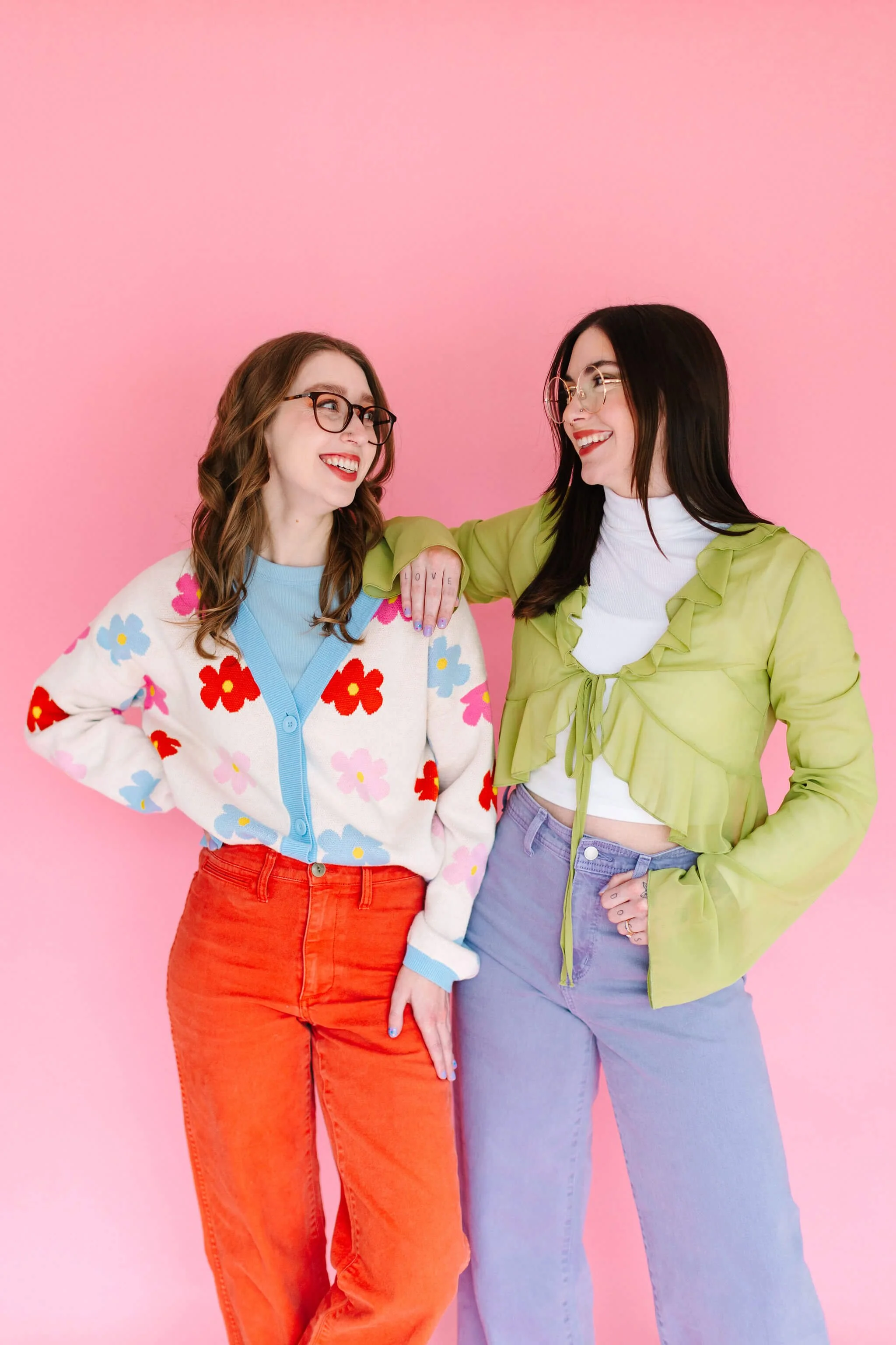 Logan and Emily stand in front of a pink wall, smiling at each other.
