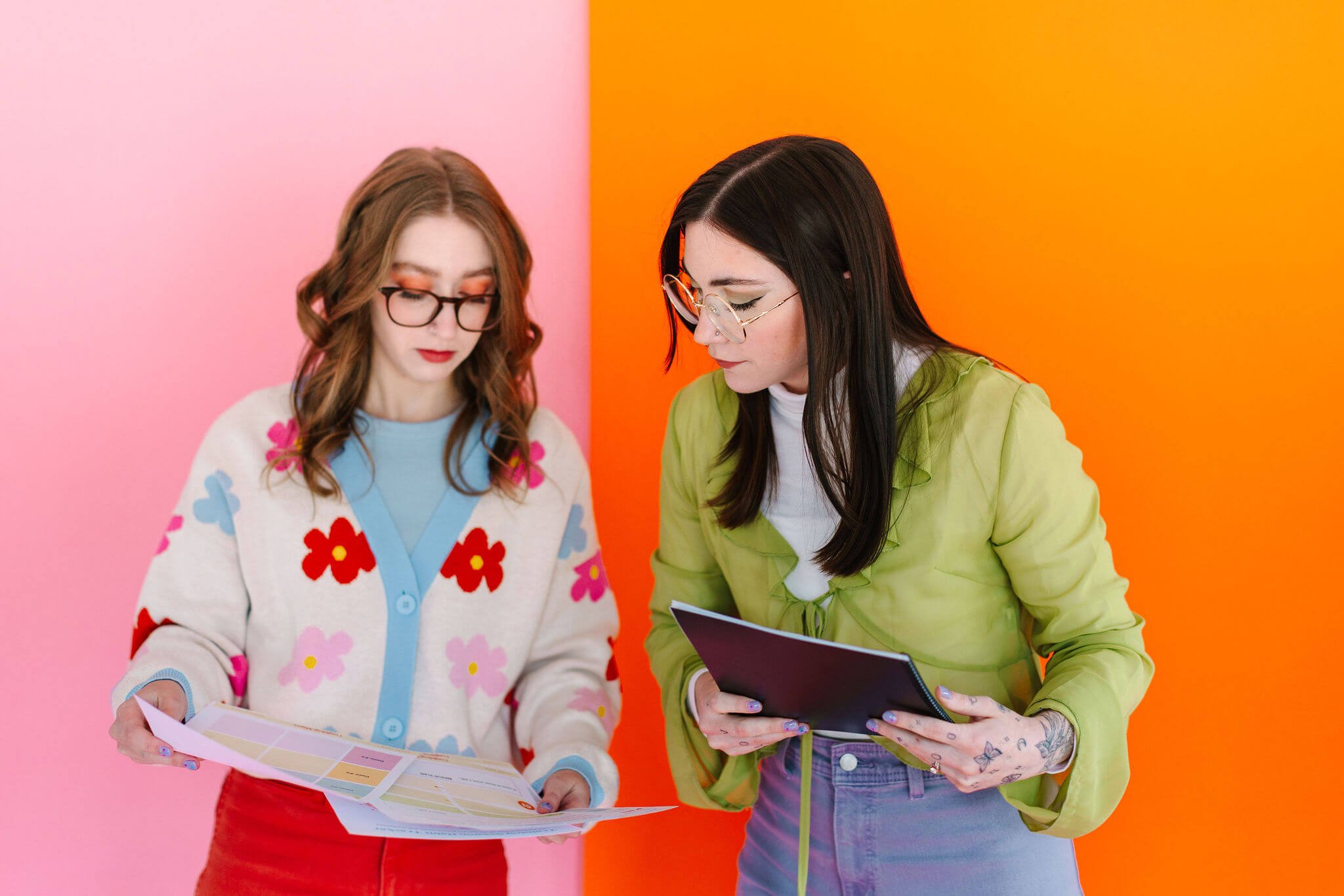 A photo of Logan and Emily standing in front of a pink and orange backdrop. They are looking at printed dog training handouts.
