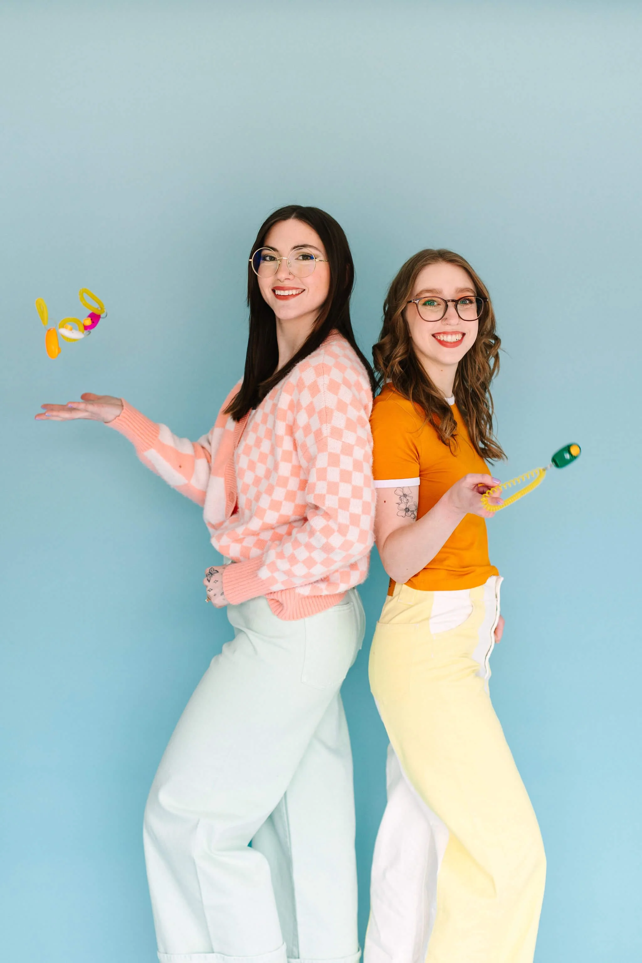 A photo of Emily and Logan, who stand back-to-back and are tossing clickers in the air.