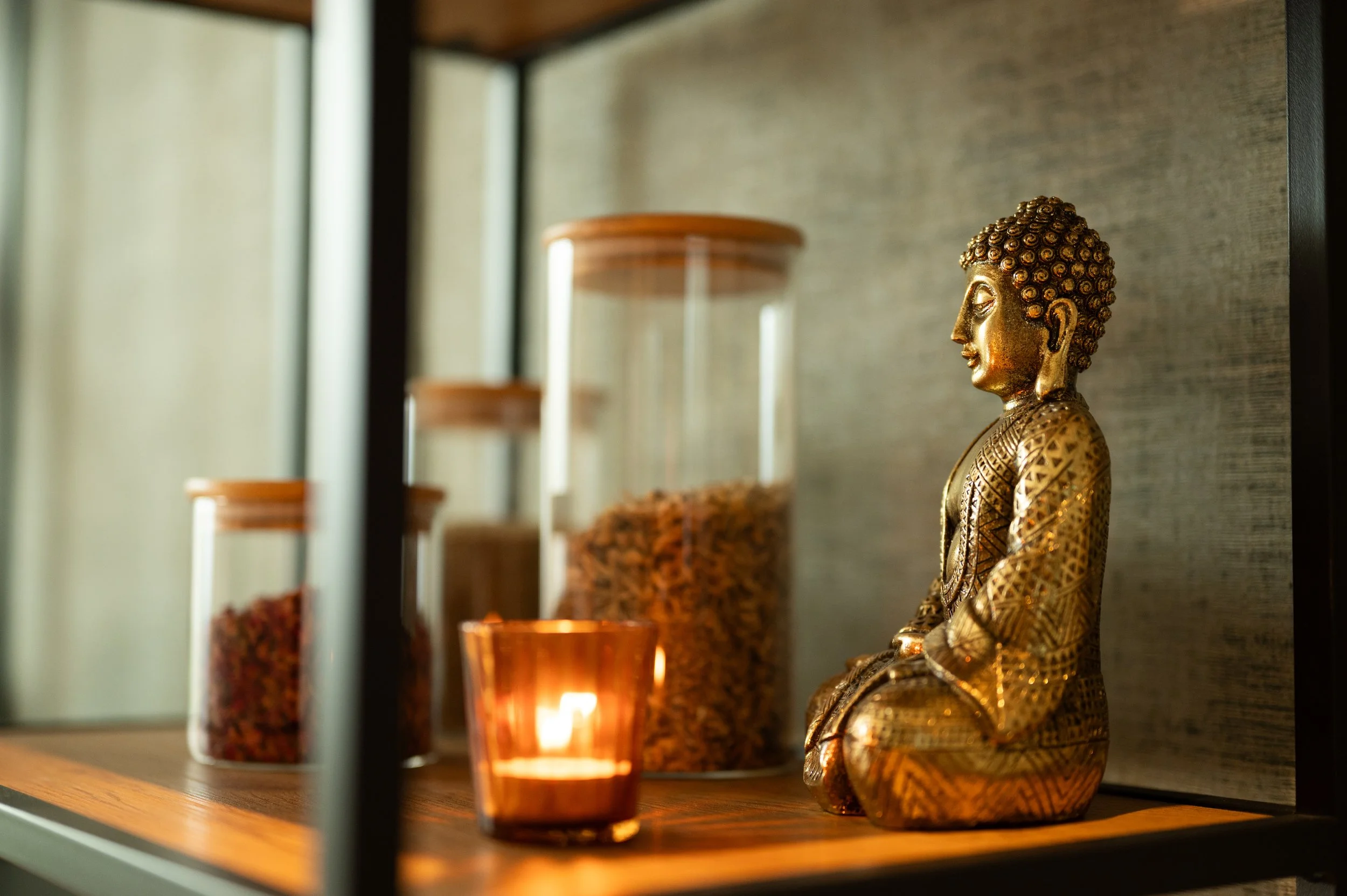 Brass Buddha, candlelight and herb jars on a shelf in the treatment room