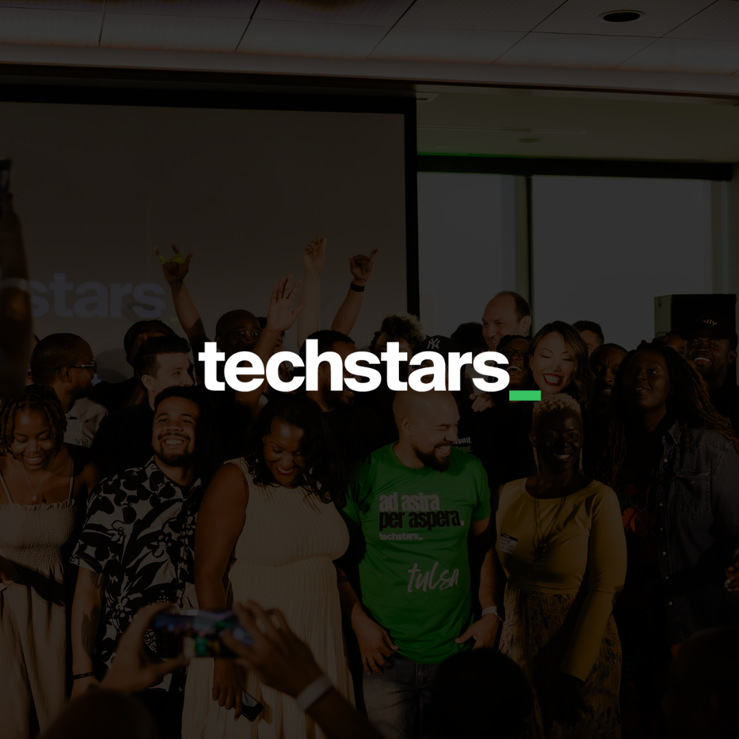 Group of diverse people celebrating at a tech event with 'techstars' logo overlay.