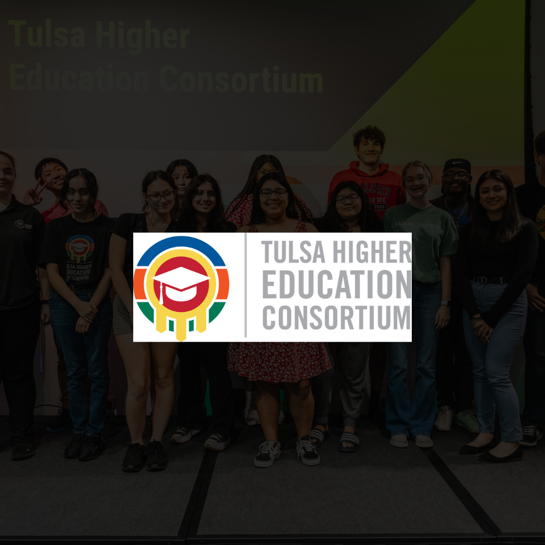 Group of diverse young students standing together on stage in front of a large screen displaying 'Tulsa Higher Education Consortium' with a logo in the foreground.