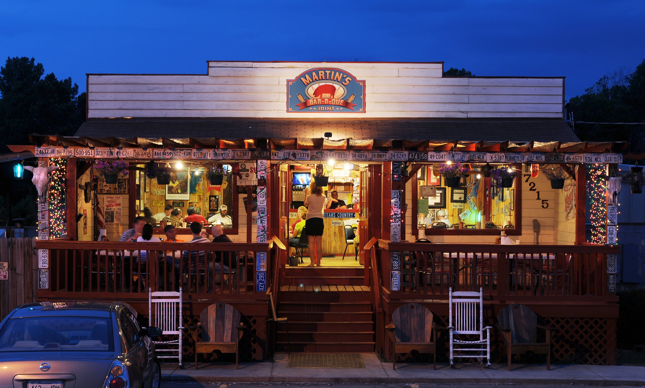Martin’s Bar-B-Que Joint restaurant exterior at night, decorated with vintage license plates and string lights