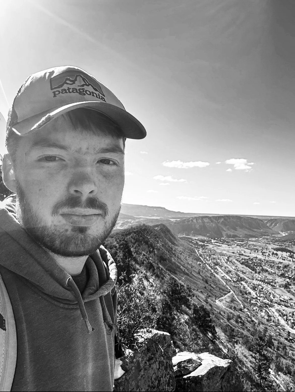 A smiling man in the fore ground with a scenic view of a town in a valley
