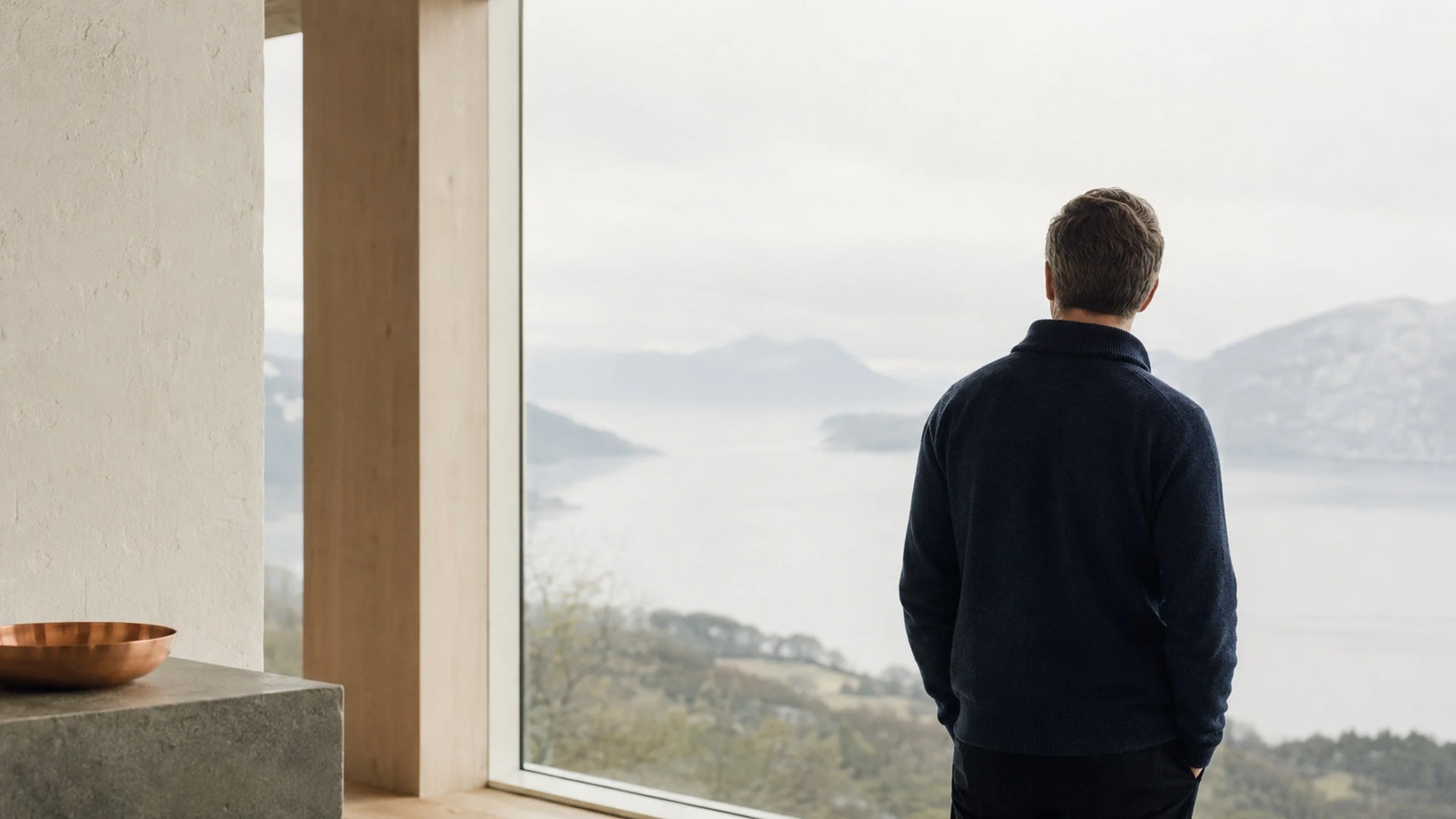 En person ser ut over fjorden fra et lyst rom.
