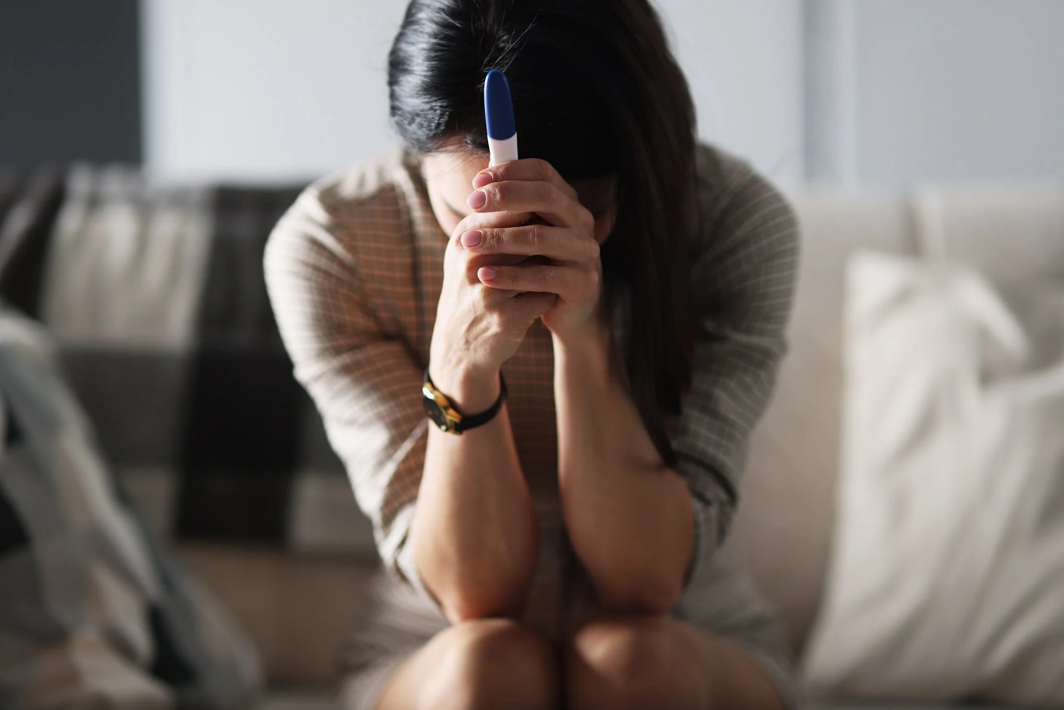Women with head in her hands holding a negative pregnancy test, representing the emotional weight of infertility and IVF