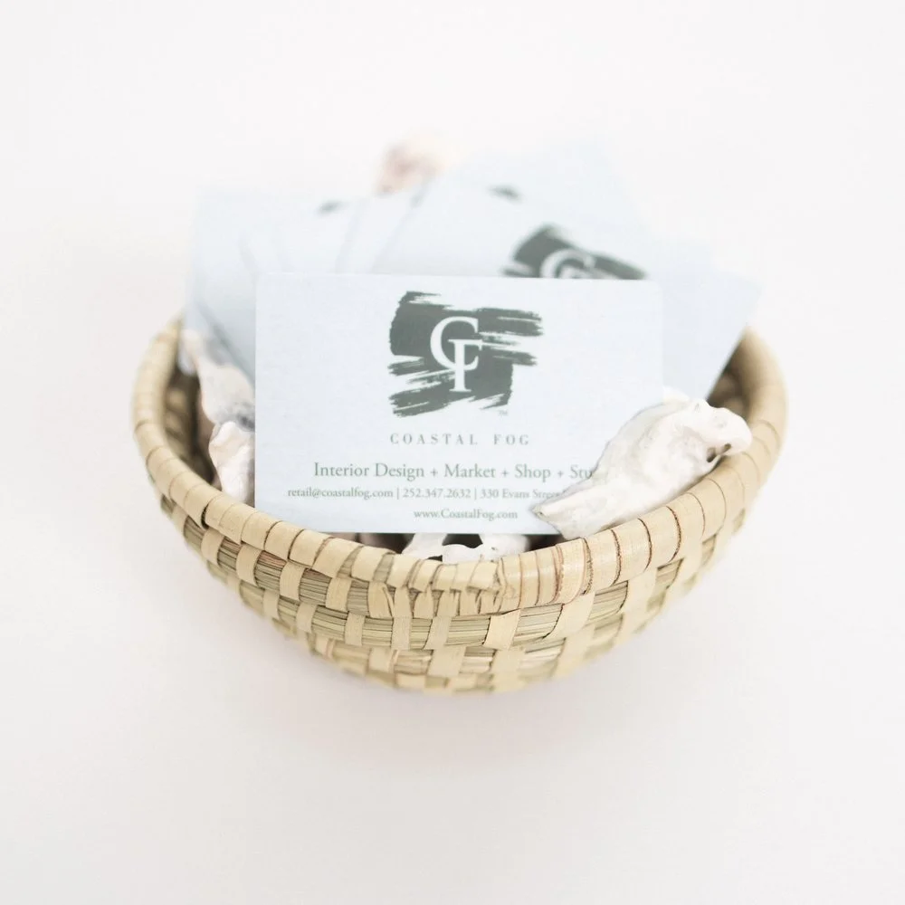 A small wicker basket containing business cards for Coastal Fog, an interior design, market, shop, and scout business.