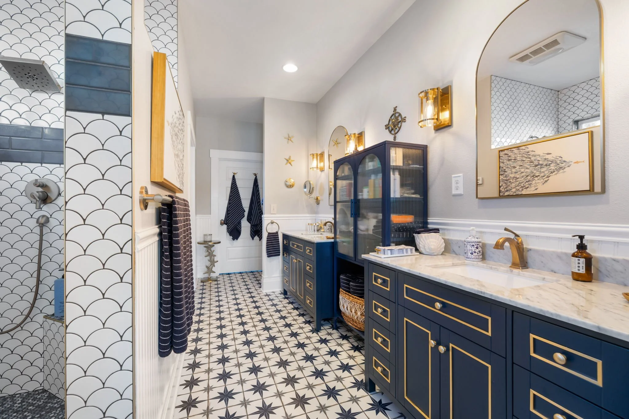 Luxury bathroom renovation featuring navy blue custom vanity, patterned tile flooring, gold fixtures, and decorative lighting.