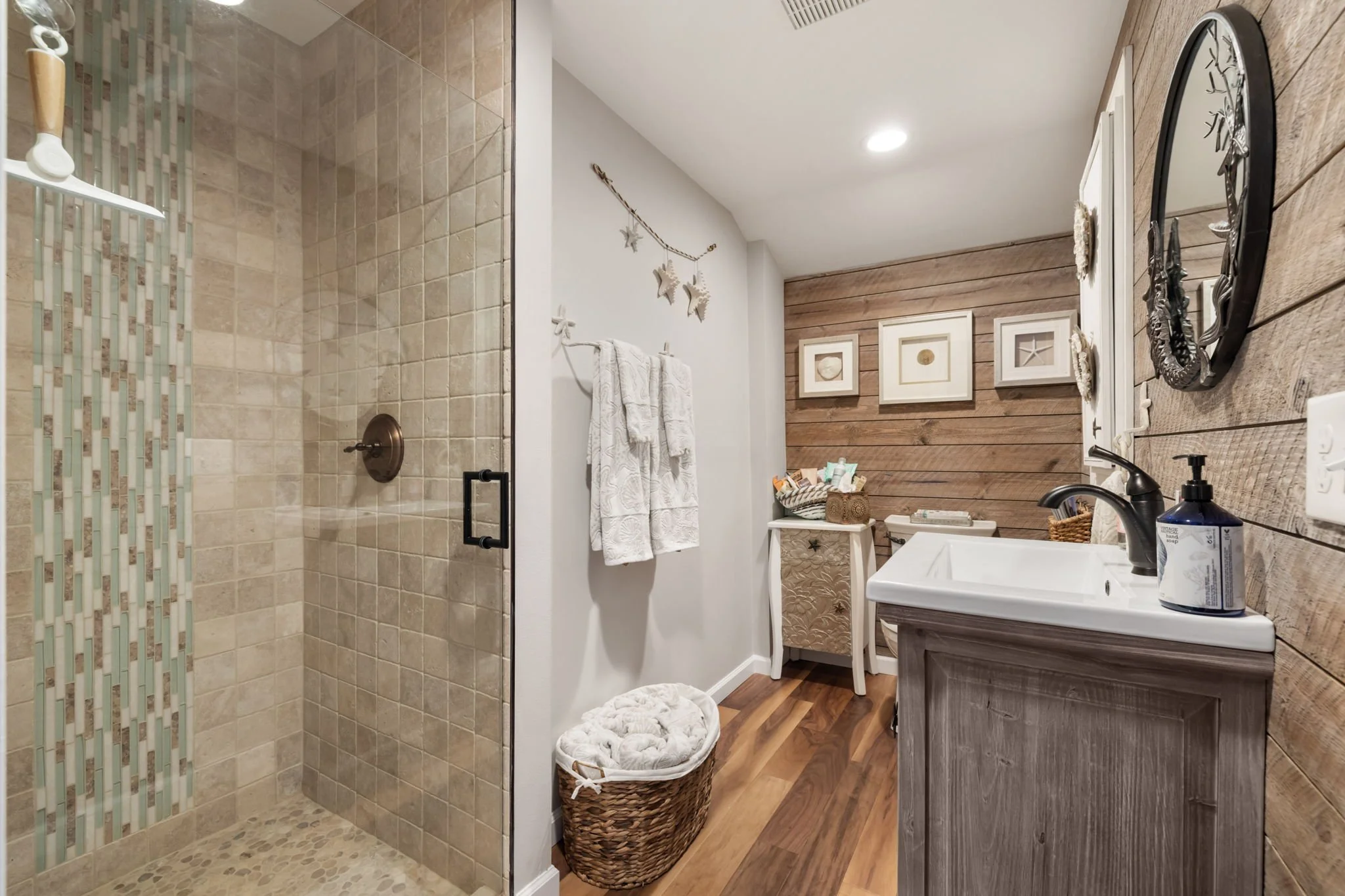 Bathroom remodel in Lakebay with wood vinyl flooring, stand-alone vanity, wood-paneled wall, and tile shower with glass door.