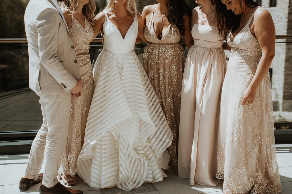  A bridal party wearing neutral beige and blush tones poses for a picture. 