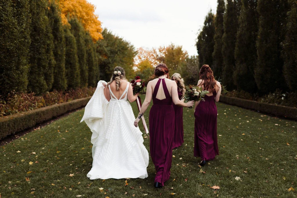 A bride and her bridal party who are wearing floor length burgundy bridesmaids dresses.