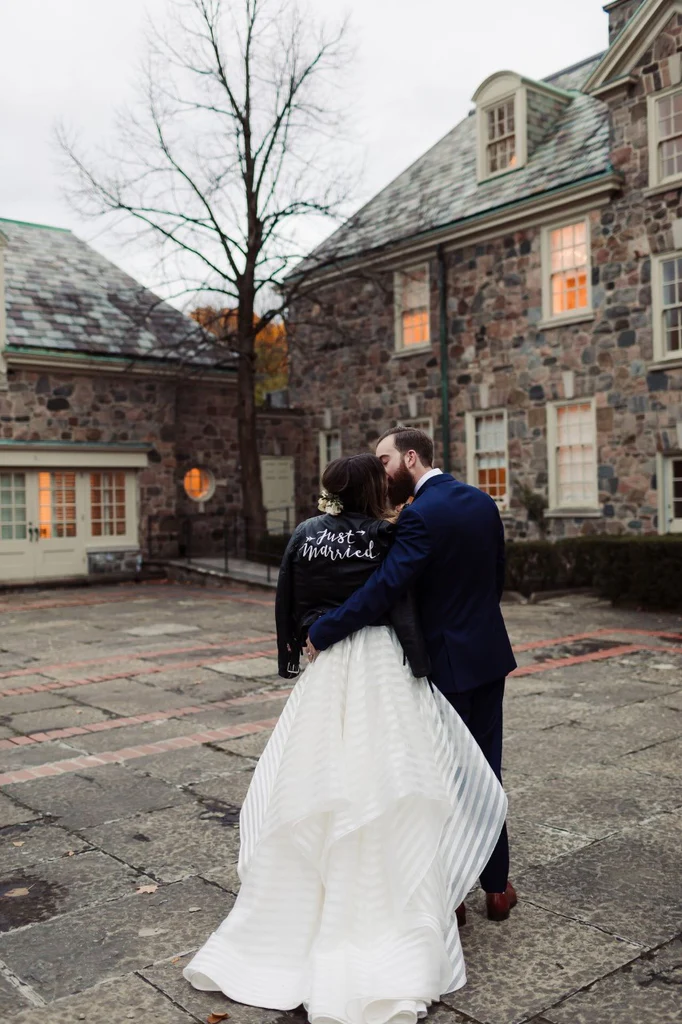 A bride and groom kiss, the bride is wearing #TheJustMarriedJacket.