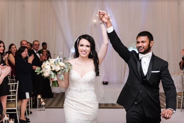 A bride and groom raise their hands after sharing a kiss and walking down the aisle.