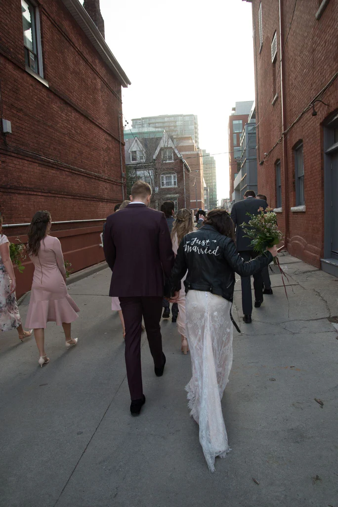 A bride sports her Just Married Jacket as her and her new husband walk down the road.