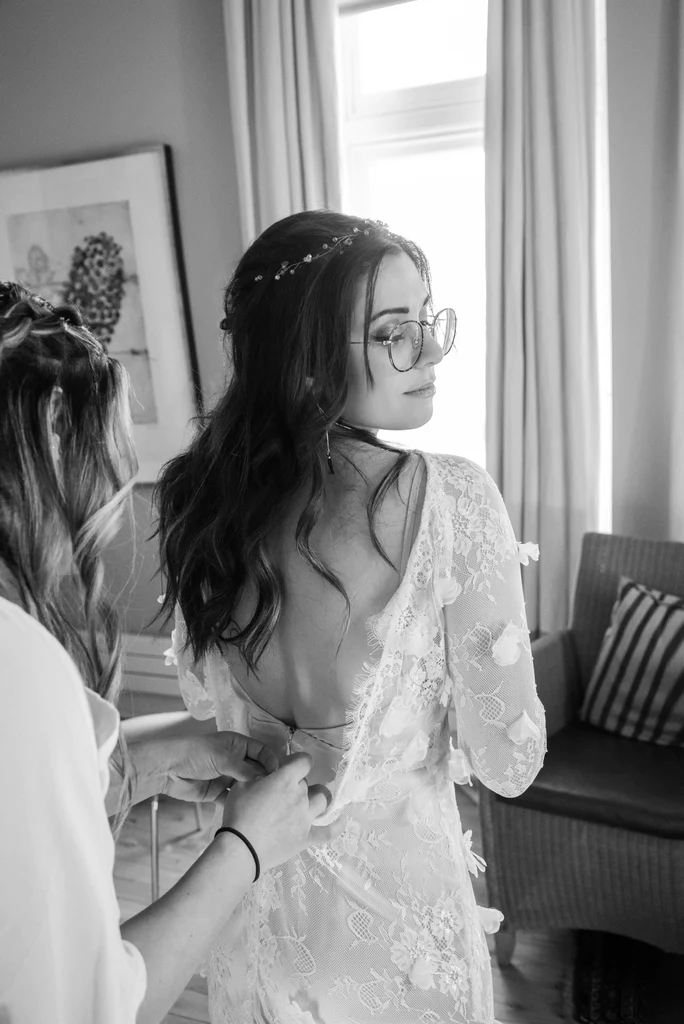 A bride getting her wedding gown zipped by one of her bridesmaids.