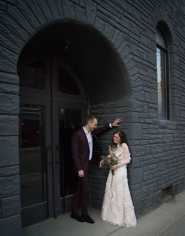 A bride and groom pose for a photo in a moody doorway.