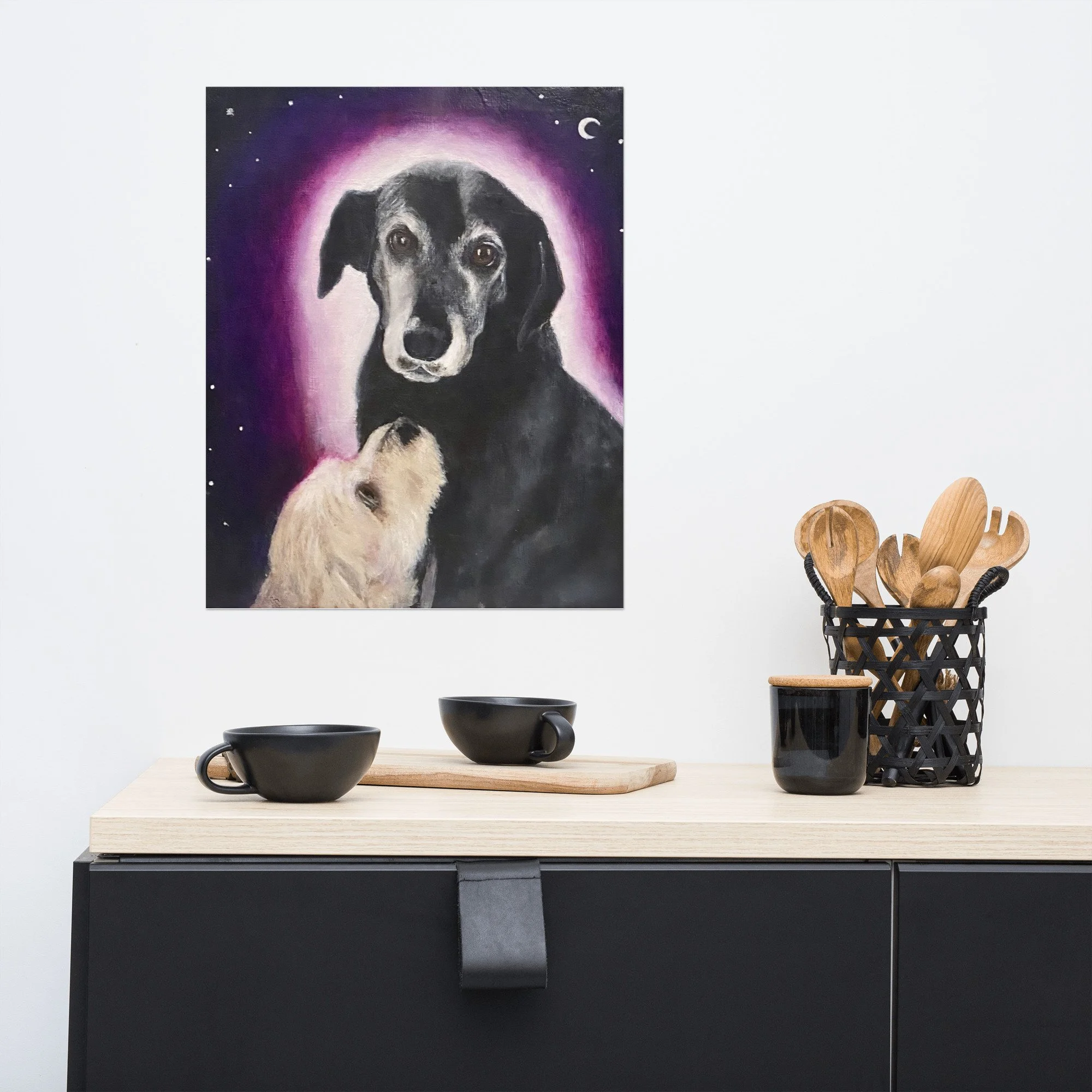 A modern kitchen with a fine art print of a dog portrait featuring an older black dog with a pink halo and a white dog looking up at them under a crescent moon by Diantha Boardman.