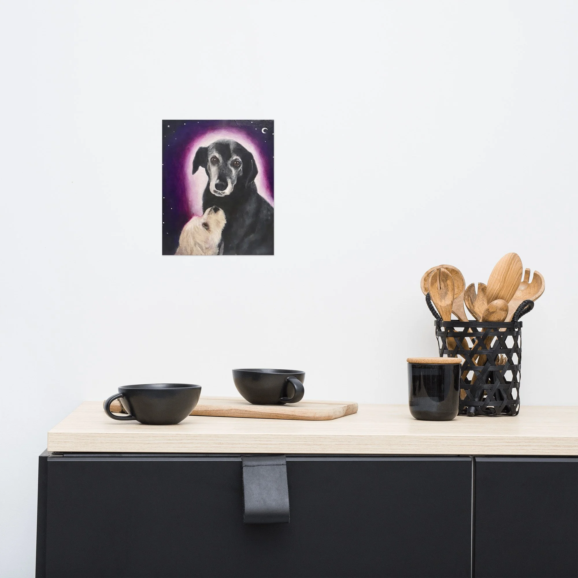 A modern kitchen with a fine art print of a dog portrait featuring an older black dog with a pink halo and a white dog looking up at them under a crescent moon by Diantha Boardman.