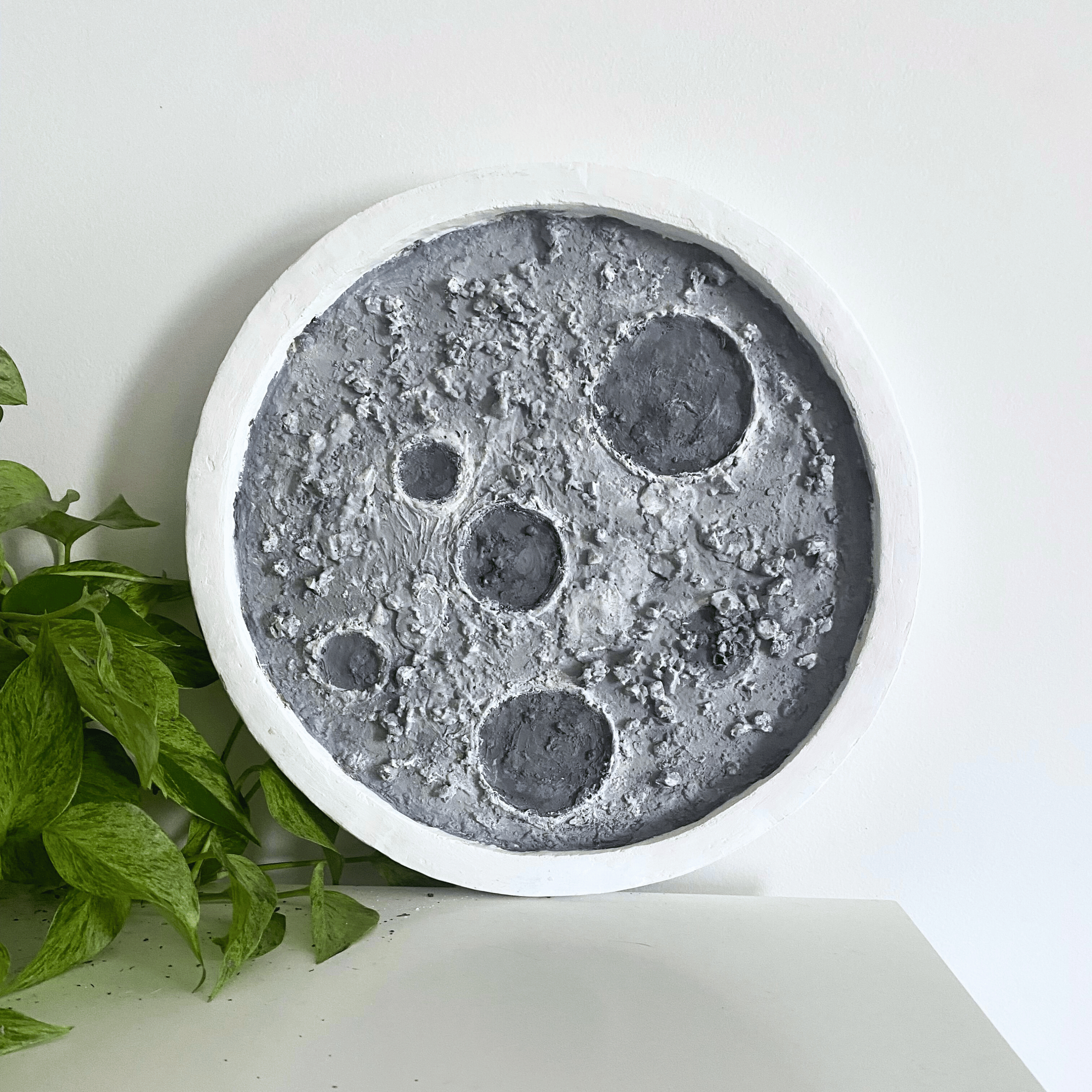 Original circular 3D moon sculpture with heavy gray texture and crater details by Diantha Boardman.