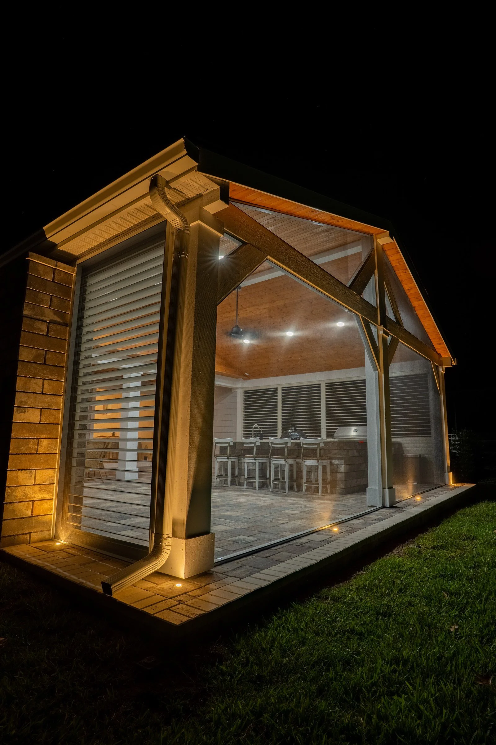 Screened cedar gazebo with custom shutters lit at night, Nocatee