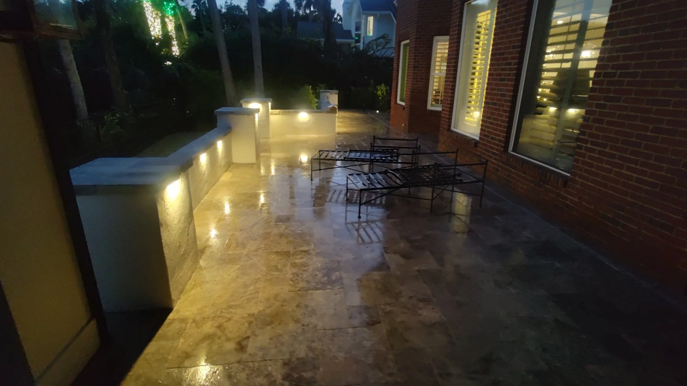 French-pattern travertine patio with lit seating walls at dusk in Sawgrass, Ponte Vedra Beach