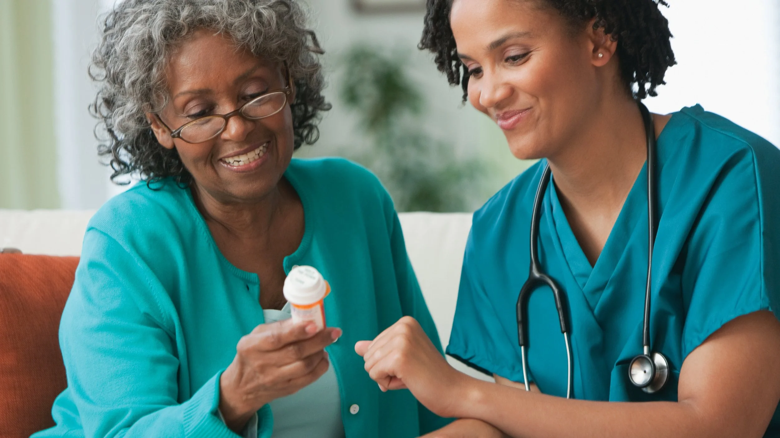 older femal patient looking at a prescription bottle and smiling with her nurse