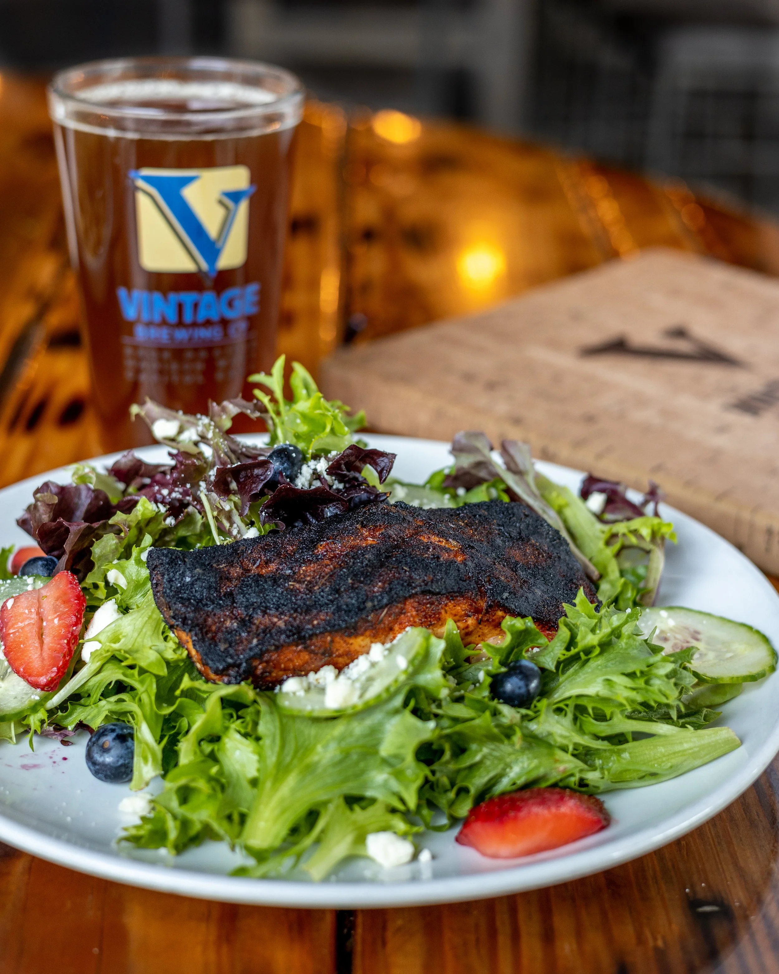 A blackened salmon salad with a beer in the background at The Vintage Brewing Company